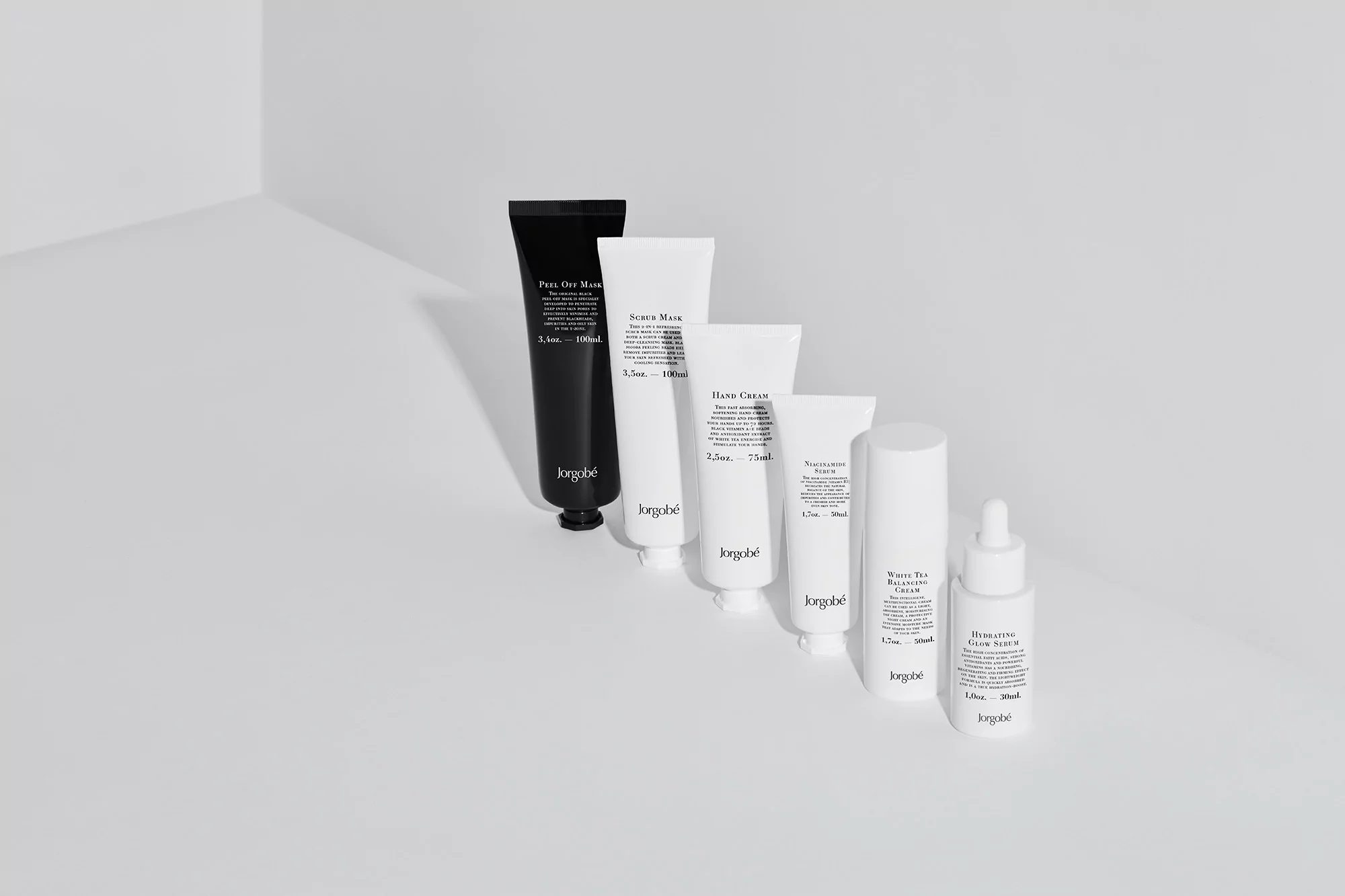 Lineup of JORGOBÉ skincare products in minimalist packaging on a white surface, featuring creams, serums, and masks in a studio setting.