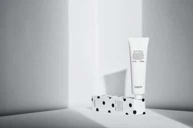 White Jorgobe scrub mask tube standing upright next to its polka dot packaging on a white studio surface.