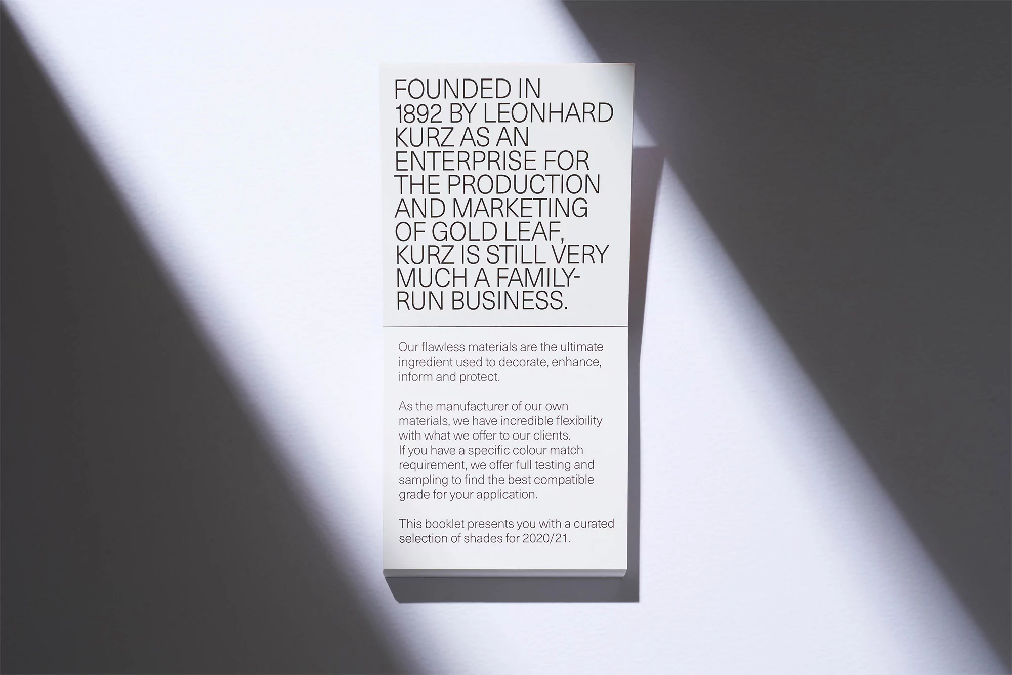 Promotional still life features an informational booklet with dark text on a white paper, presented under a directional light source.