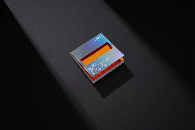 Close-up studio shot of a Kurz Collection swatch book with iridescent cover, orange interior, and crisp, dark shadows. Product photography.
