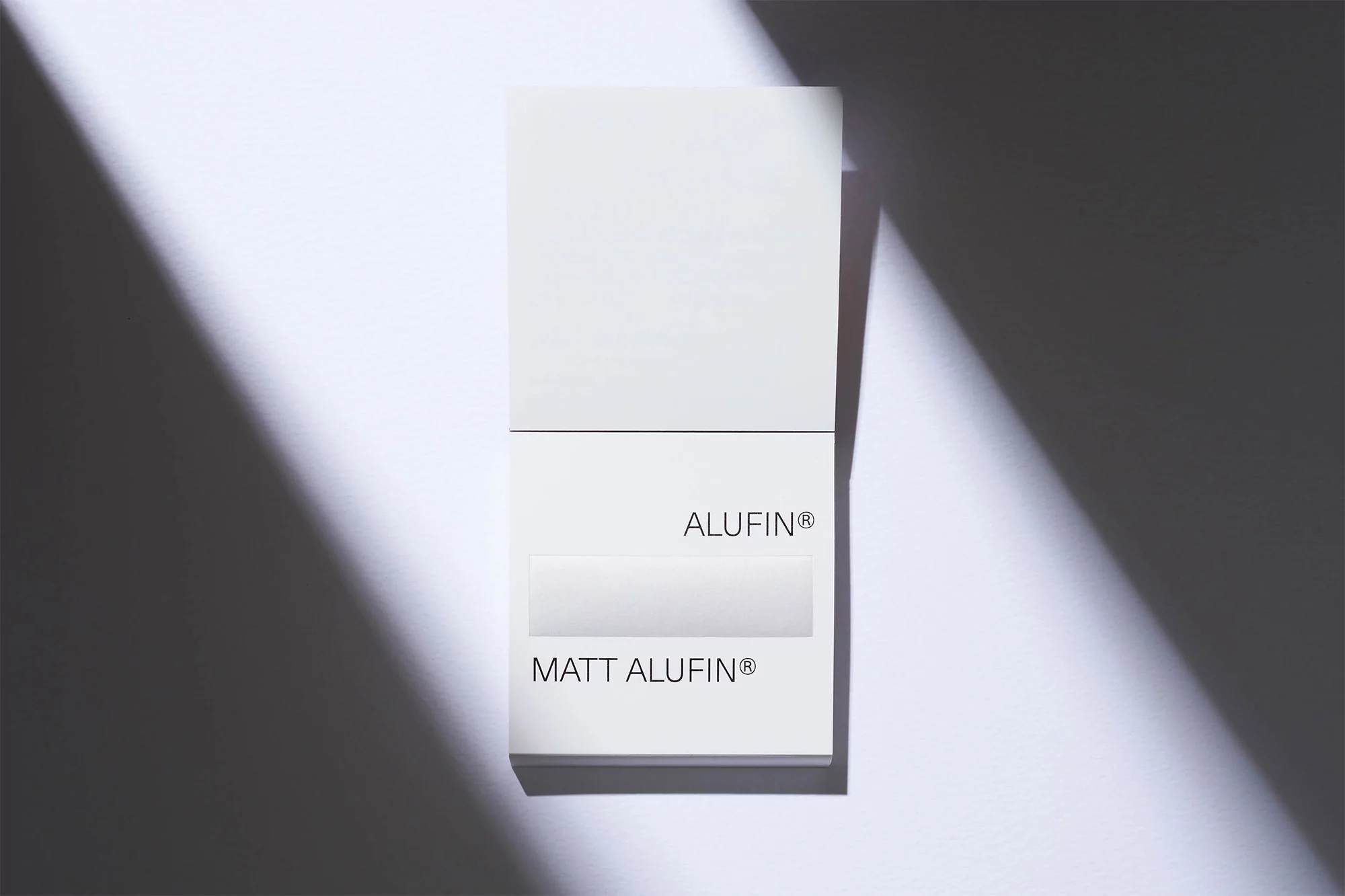 Stack of white paper or card stock with 'ALUFIN' and 'MATT ALUFIN' text, set against a white background with a shadow overlay.