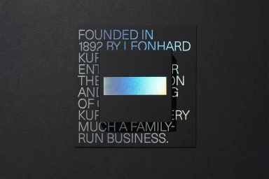 Close-up top-down view of stacked dark paper cards featuring iridescent foil typography for Kurz brand identity