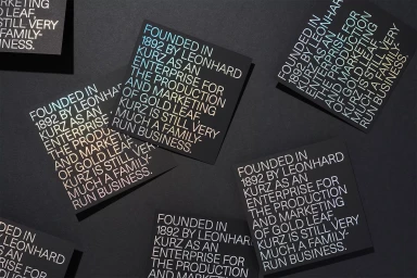 Black square cards featuring foil-stamped typographic text arranged on a dark grey textured surface
