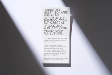 Vertical composition of a white paper booklet with black typography under diagonal harsh light casting dark shadows.