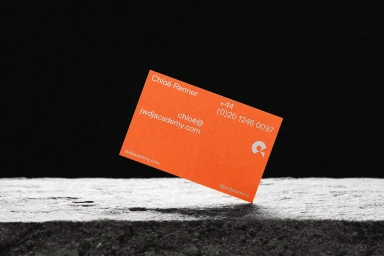An orange business card angled on a textured grey stone surface against a dark background for St. Leo brand identity.