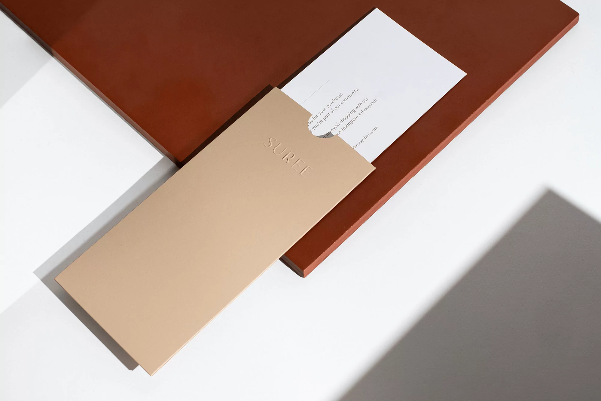 Branded stationery and envelope with embossed logo resting on a terracotta panel against a white surface