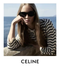 Model Rebecca Leigh Longendyke wearing dark sunglasses and a black and white striped cardigan by the ocean.