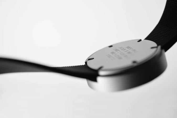Close-up of a black watch band connected to a round, silver watch face with engraved text, set against a bright white background.