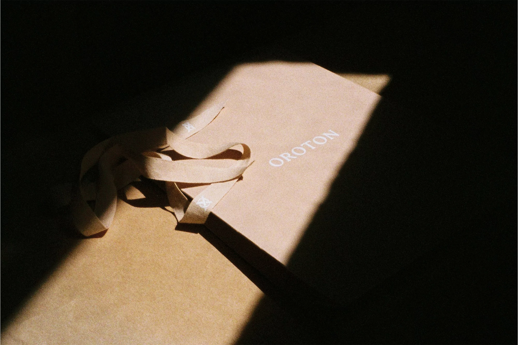 Beige Oroton shopping bag with light beige ribbon and window lighting creates a minimalist, high-contrast product shot.