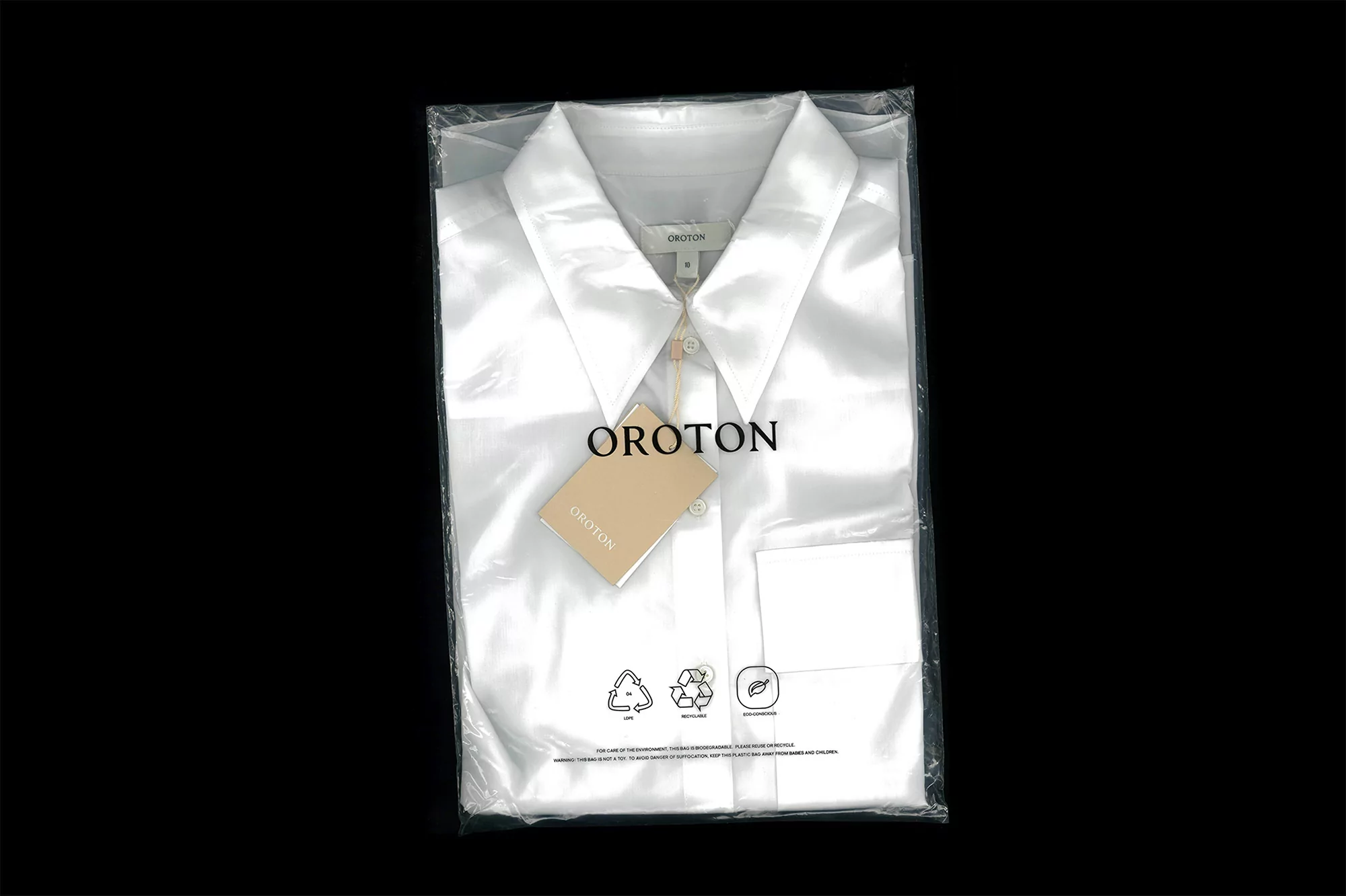 Folded white button-down shirt inside clear plastic packaging with an attached brand tag. Studio shot on black background.