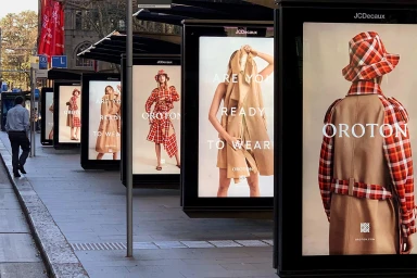 Row of illuminated outdoor advertising light boxes displaying Oroton fashion campaigns along a city sidewalk
