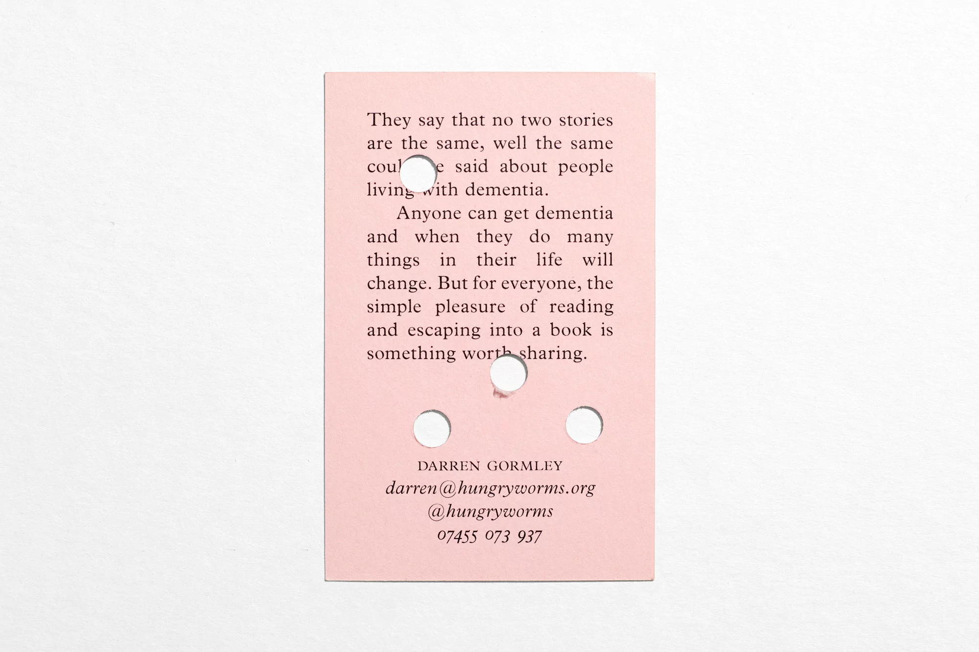 Close-up of a pink paper card with black text about dementia and the pleasure of reading, featuring Darren Gormley's contact information.