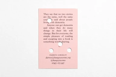 A rectangular pink printed card with black text and four circular punched holes resting on a plain white surface