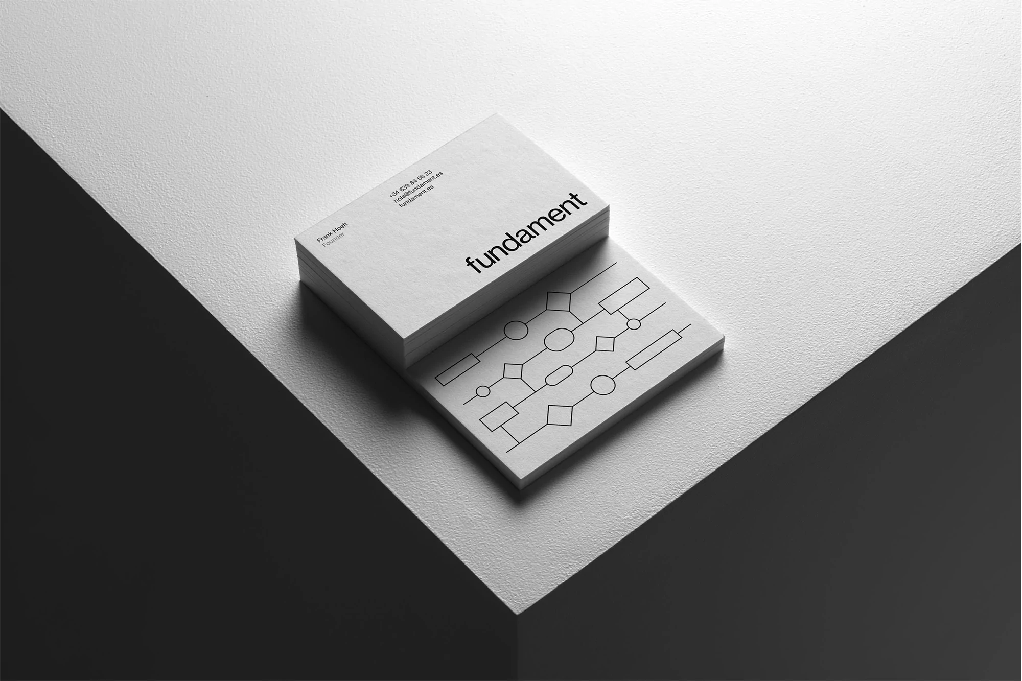 Stack of white business cards with black typography and geometric line art resting on an angled white and dark grey surface.