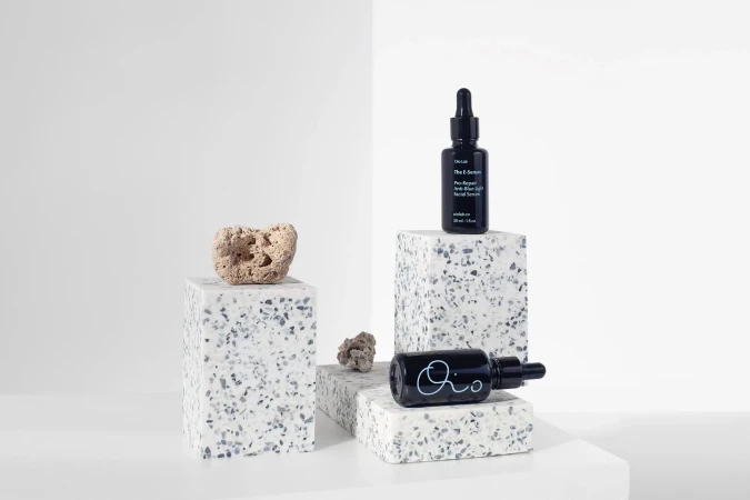 Product shot of skincare serum bottles on a geometric display with minimalist white background in a beauty or fashion context.