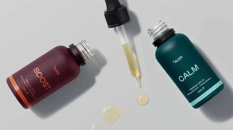 Two dropper bottles labeled BOOST and CALM with a glass dropper and spilled oil droplets on a grey background