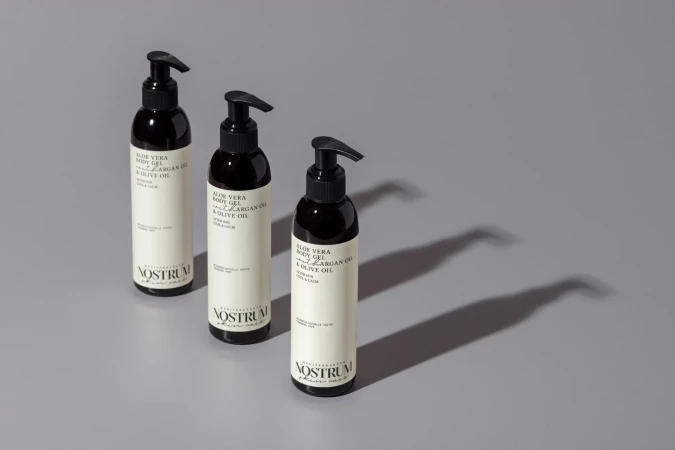 Three dark amber pump bottles of body gel arranged diagonally on a smooth grey surface casting long sharp shadows