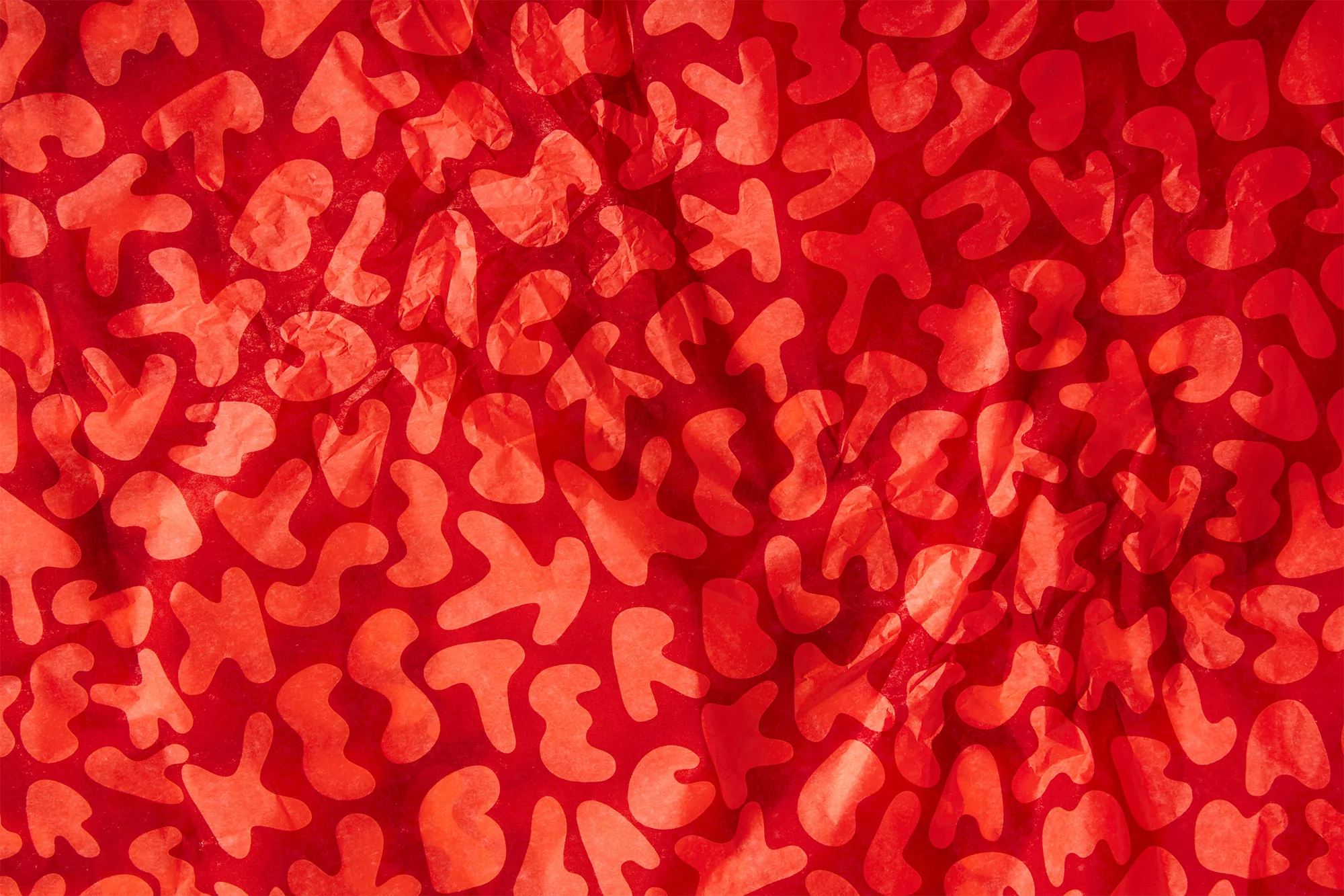 Close-up shot of crumpled red tissue paper with a subtle pattern for abstract backgrounds or textures, creating an eye-catching visual effect.