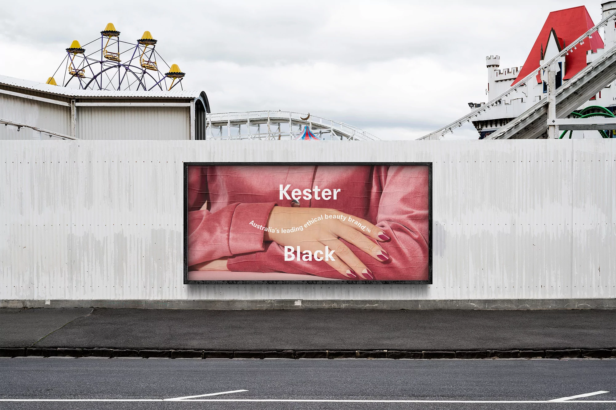 Billboard advertises Kester Black beauty brand with hand displaying manicure. Fairground and roller coaster in background against grey sky.