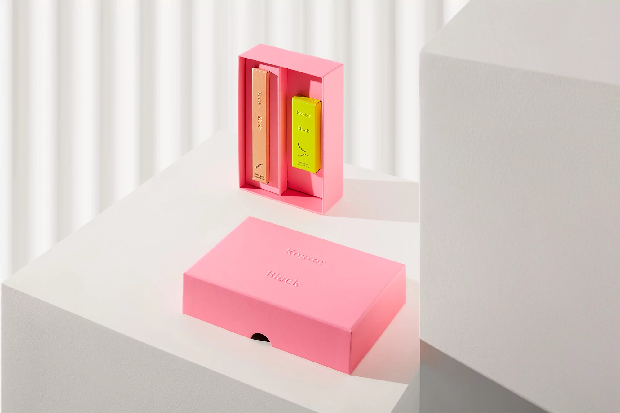 Stacked pink Kuston Black boxes showcase product packaging in pink, orange, and yellow hues against a white wall background.