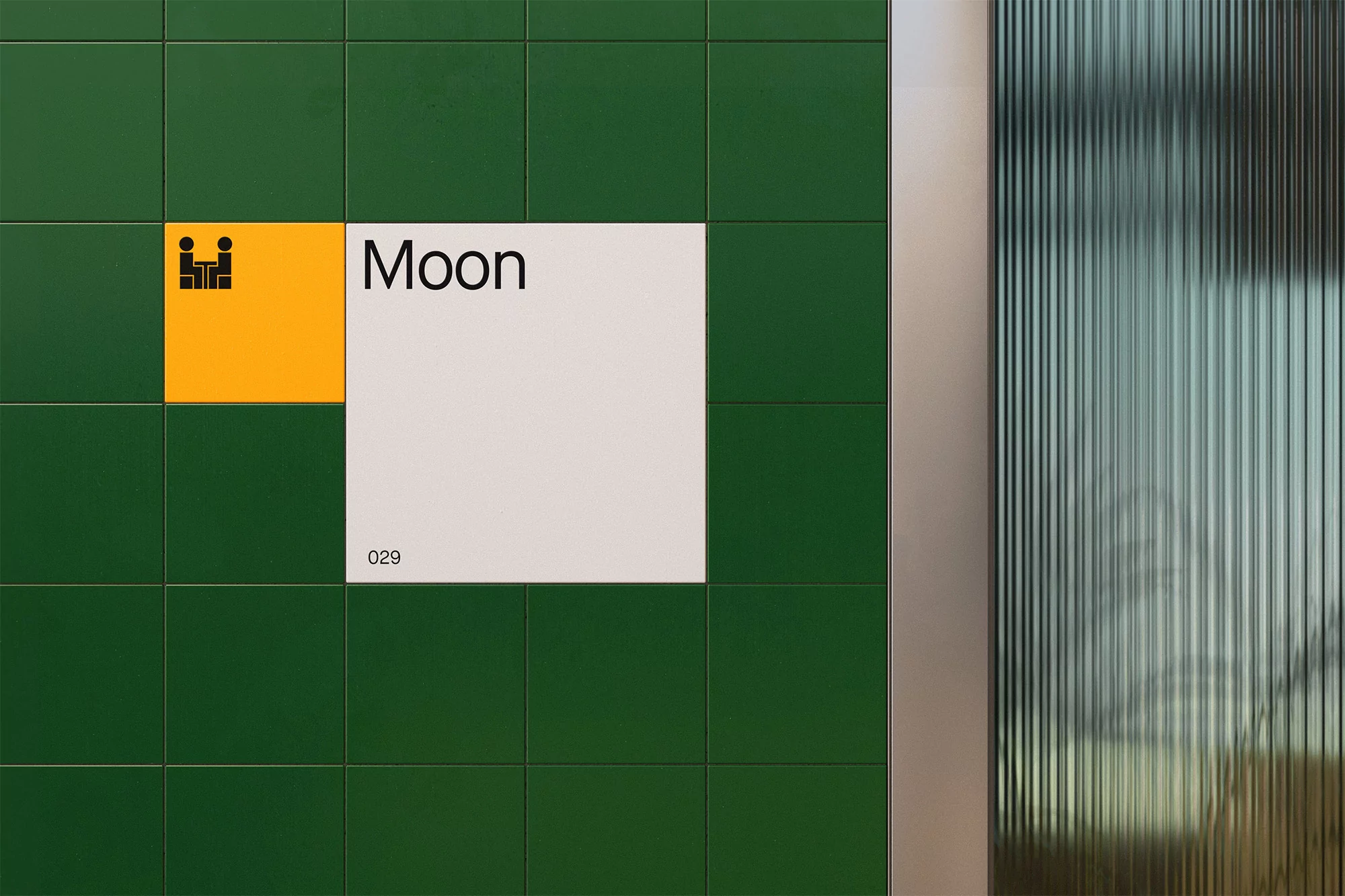 Close-up of a green tiled wall with a yellow and white square with the text 'Moon' and the number '029' next to a fluted glass panel.