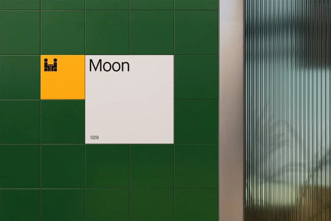 Close-up of a green tiled wall with a yellow and white square with the text 'Moon' and the number '029' next to a fluted glass panel.