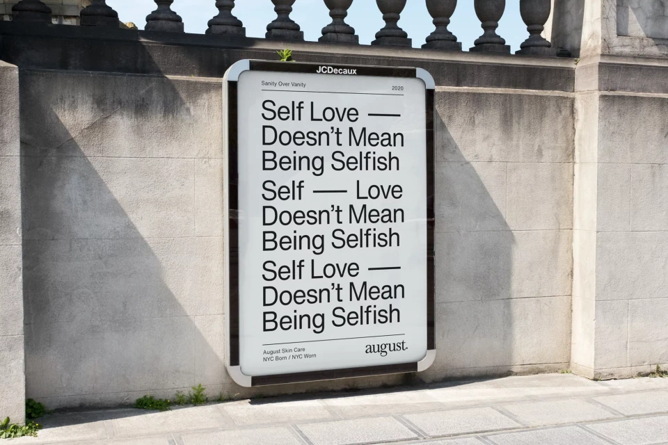 Outdoor advertising billboard featuring a text-based message about self-love in black font, set against a textured concrete wall.