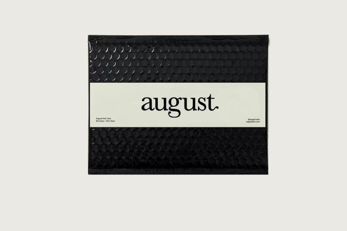 Close-up studio shot of a black August brand padded envelope with a white label, presented on a clean white background.