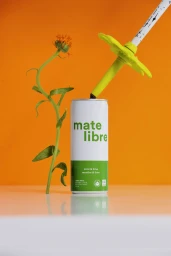 Mate Libre beverage can with a green straw and orange flower against a bright orange background