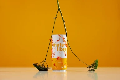 A Mate Libre beverage can styled with natural foliage and dried petals against a solid yellow background.