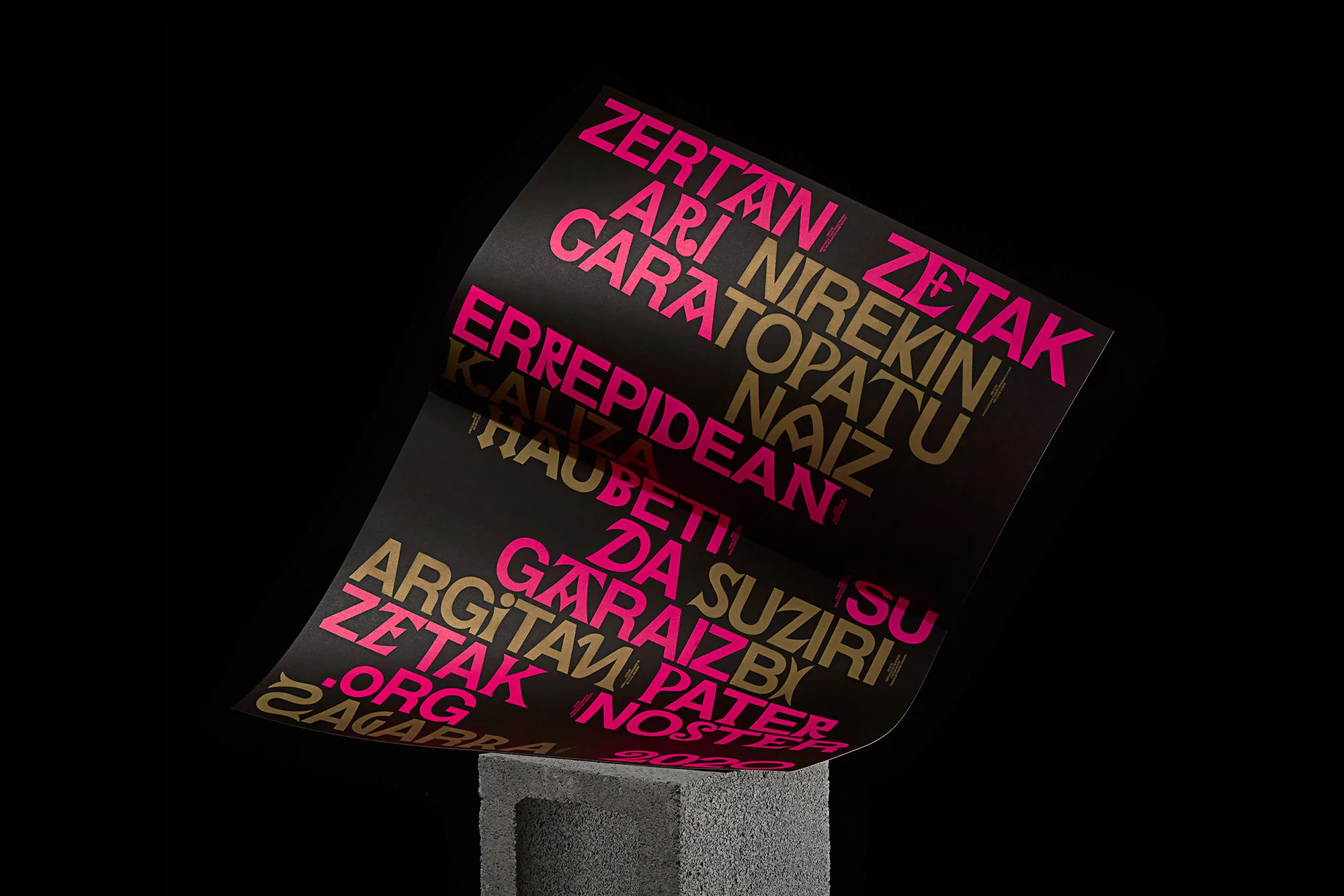 Eye-level shot of a black poster with gold and pink text resting on a gray concrete block, set against a dark black studio backdrop.