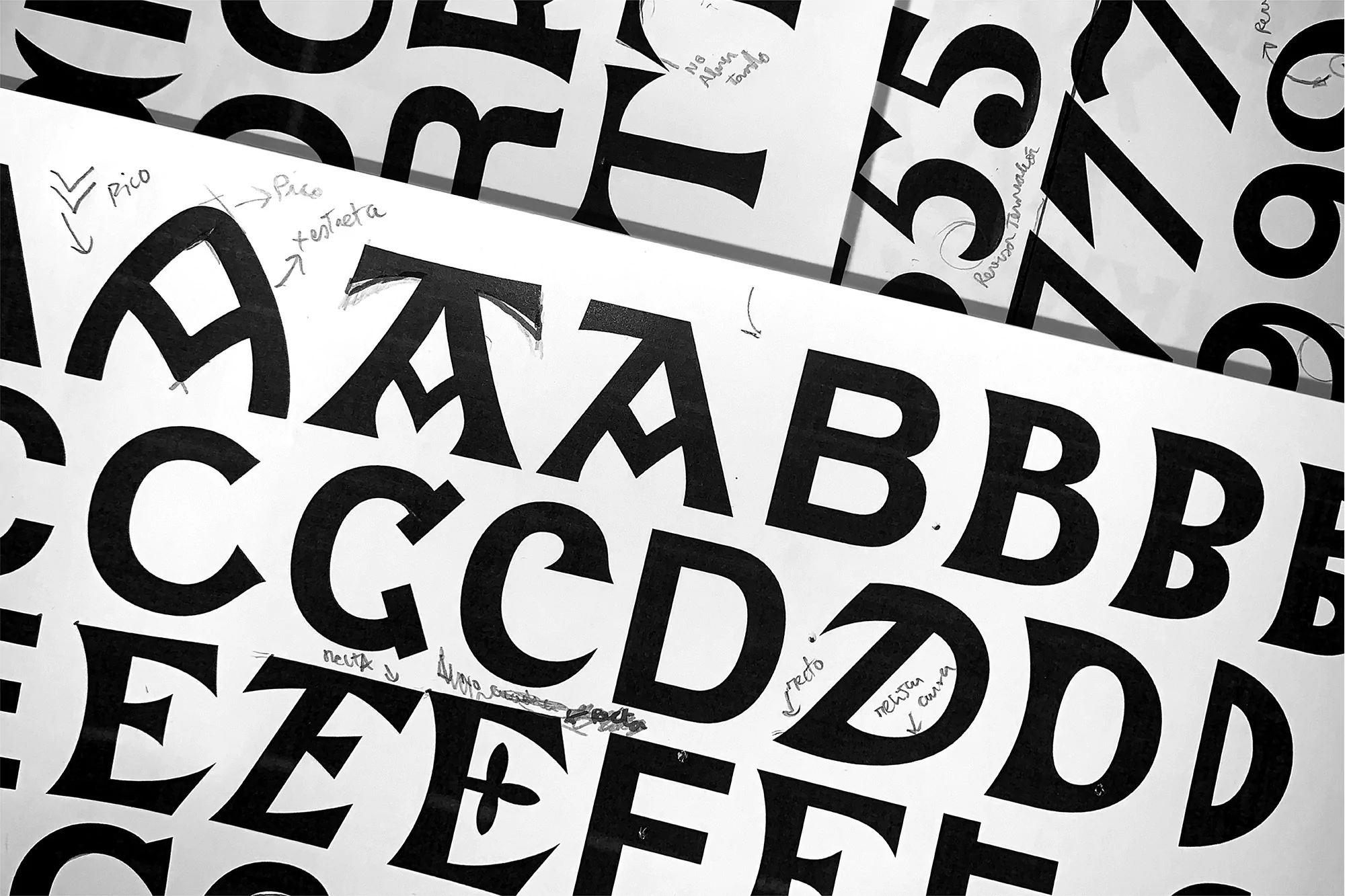 Black-and-white image displaying uppercase letters on white sheets of paper, creating an abstract composition focused on typography.