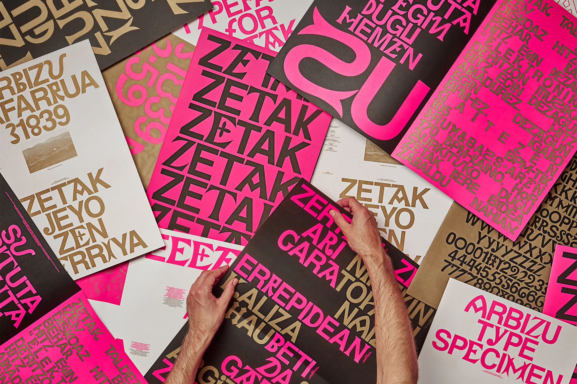 An overhead shot showcases hands arranging vibrant posters featuring large, bold typography in pink, black, and gold against a neutral background.