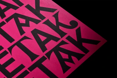 Bold black typography repeating the word ZETAK on a vibrant pink textured paper sheet shot from an angled perspective against a dark background