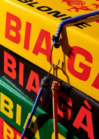 Close-up of stacked 'Bière' branded boxes secured with blue and orange bungee cords, showcasing a product-focused commercial aesthetic.