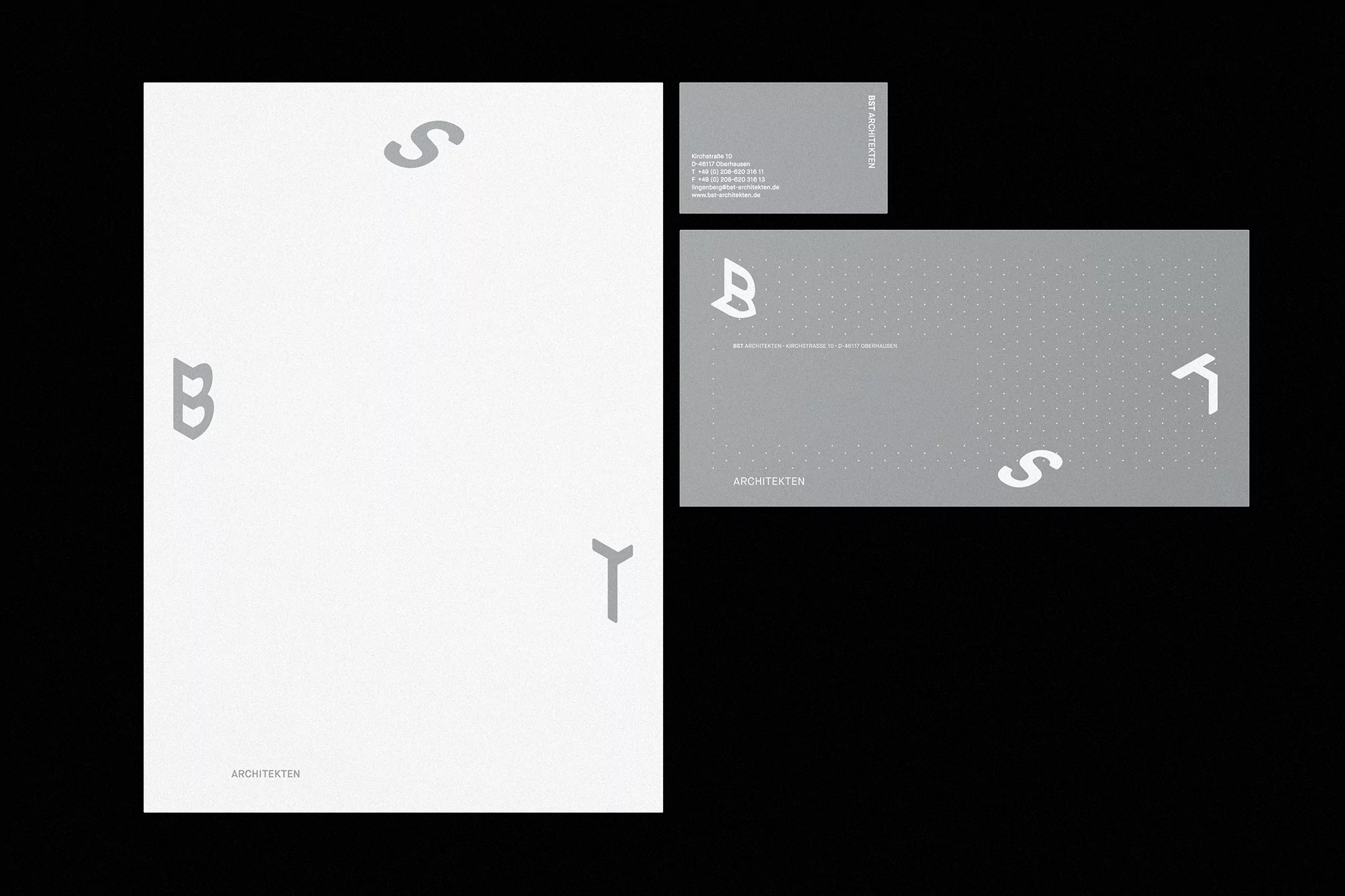 Letterhead, business card, and envelope mockups with architectural logo and contact information in gray tones against a black background.