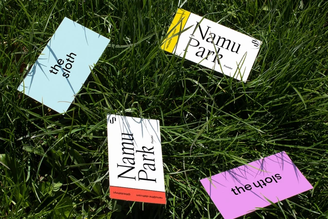 Four printed business cards scattered across green grass blades in bright natural sunlight.