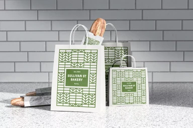 White paper shopping bags with green geometric patterns and Sullivan St Bakery branding holding baguettes