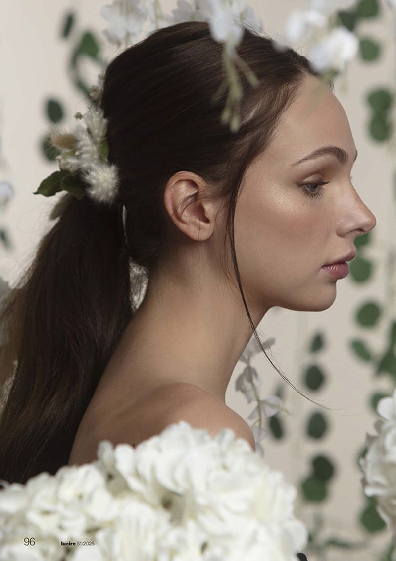 Portrait of a young woman with dark hair in a ponytail, decorated with white flowers, posing against a floral background in a studio.