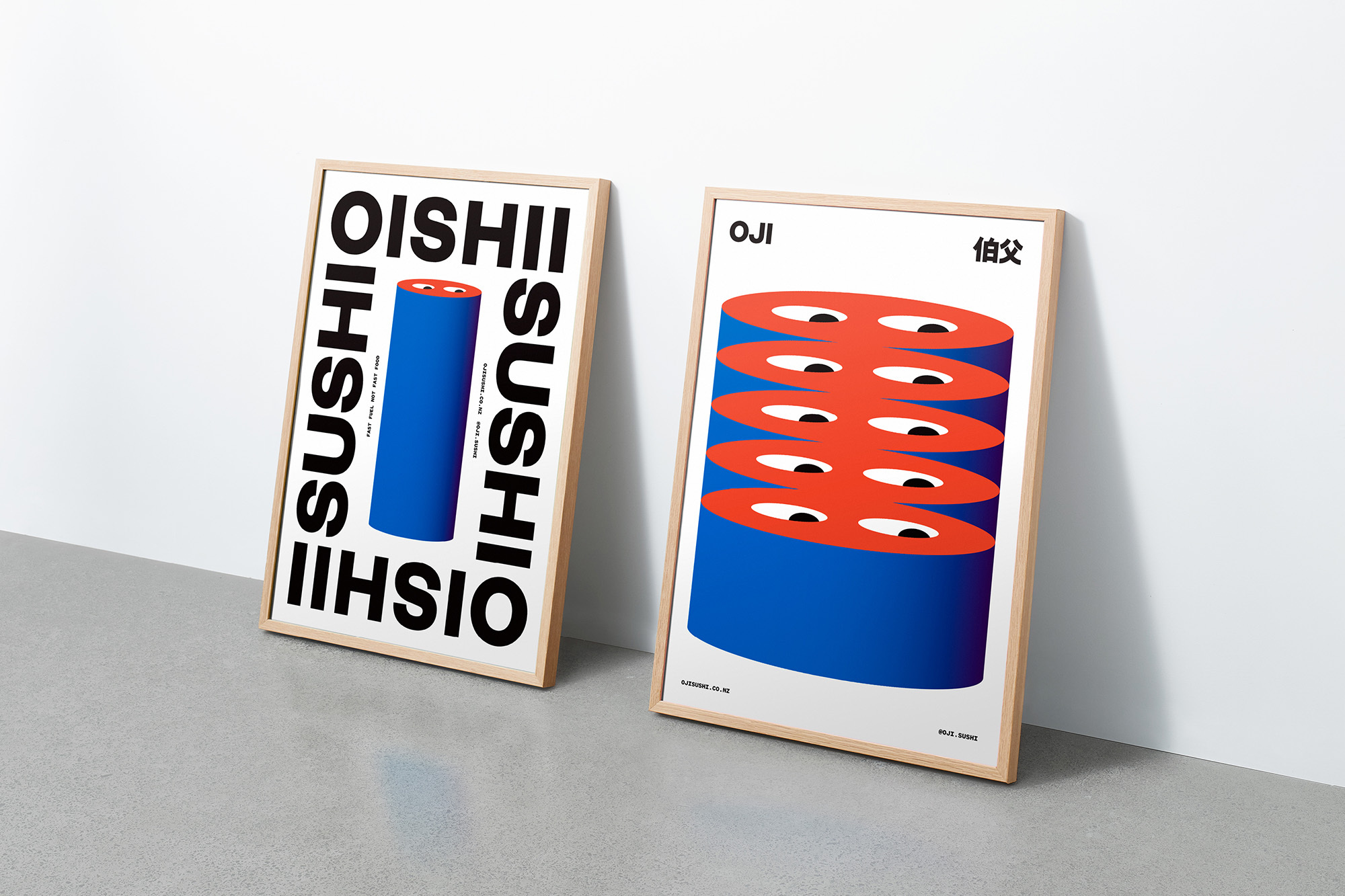 Two framed posters lean against a white wall, featuring abstract designs with cylinders and bold typography in black, red, and blue.