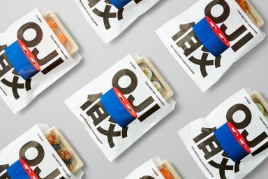 Flat lay of OJI sushi packaging bags with bold typography and blue tape rolls on a grey background