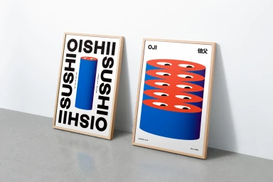 Two framed graphic posters leaning against a white wall on a grey floor, featuring bold Oishii and Oji branding with blue and red cylinders.