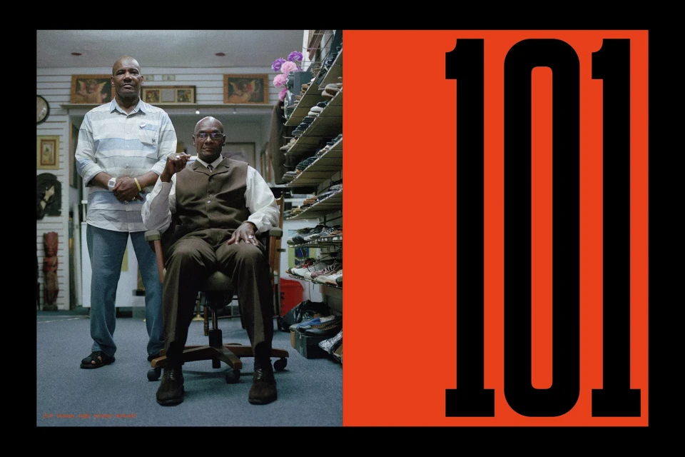 Two adult African-American men pose indoors in front of a shoe rack, next to black numbers on orange and black background.
