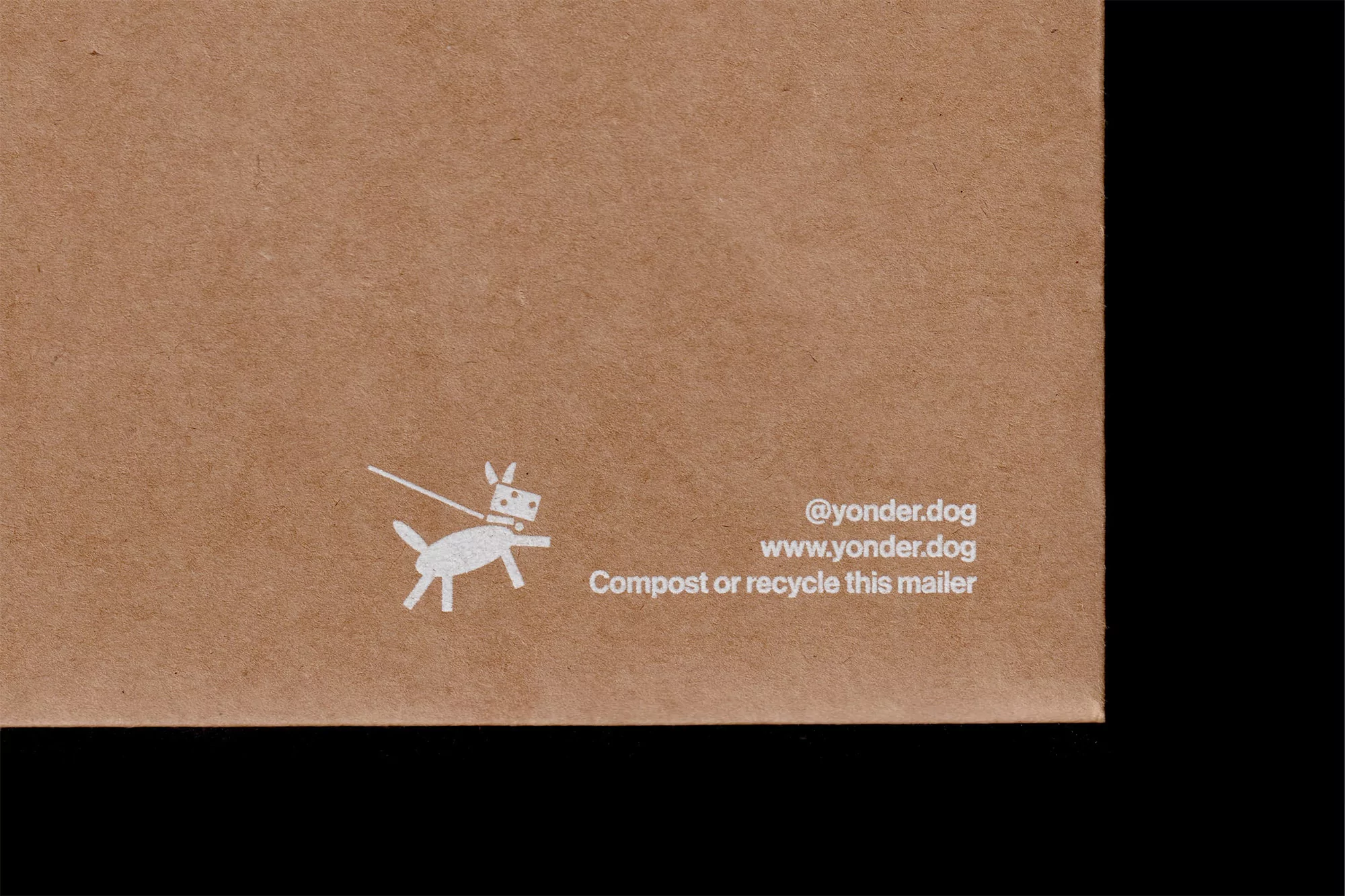 Close-up on a brown cardboard mailer featuring a white cartoon dog graphic, website address, and recycling instructions in simple design.