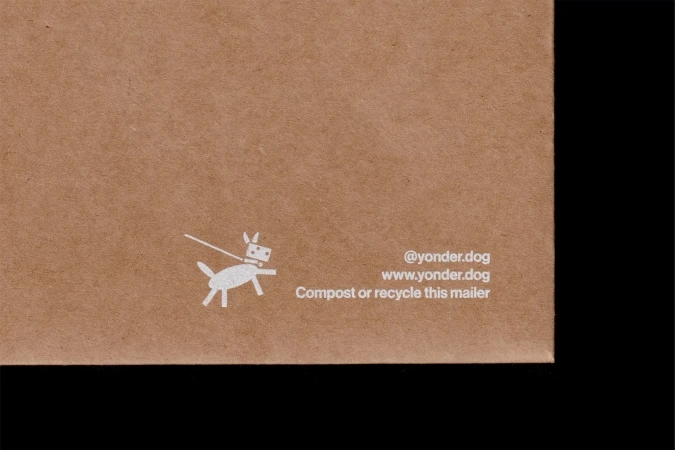 Close-up on a brown cardboard mailer featuring a white cartoon dog graphic, website address, and recycling instructions in simple design.