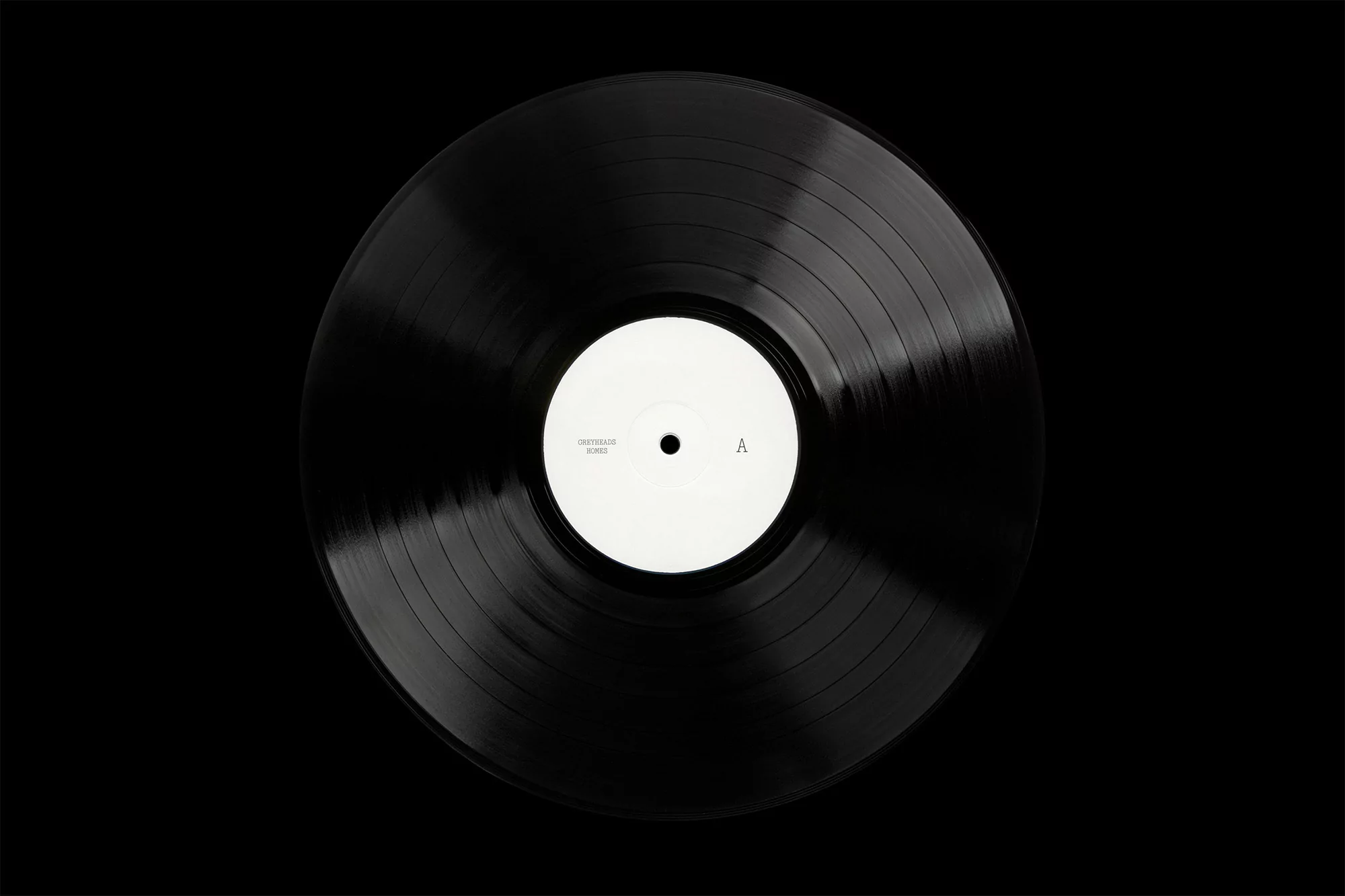Overhead studio shot of a black vinyl record with a white center label on a black backdrop, showcasing music and sound.