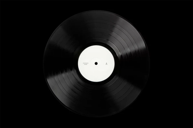 Overhead studio shot of a black vinyl record with a white center label on a black backdrop, showcasing music and sound.