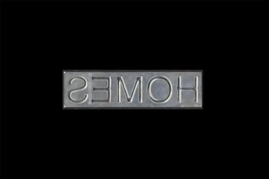 Embossed metallic letterpress stamp spelling out reflected text against a stark black background.