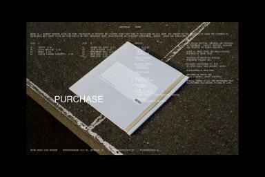 White vinyl record jacket and liner notes resting on a rough concrete surface with overlaid white typography.