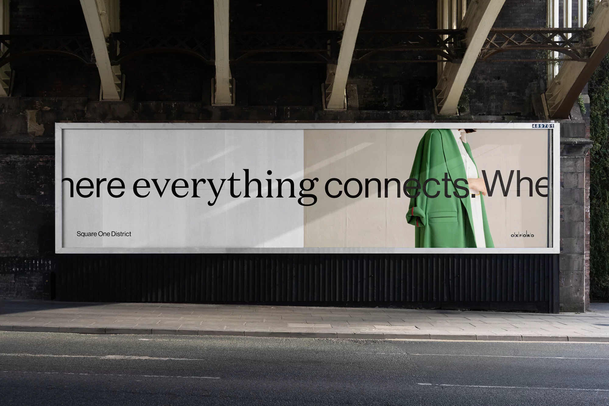 Billboard advertising campaign under a bridge featuring a woman in a green coat and black text on a white background.